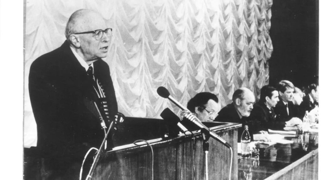 (Sakharov à la tribune de la conférence constitutive de « Memorial », le 28 janvier 1989. A droite : A. Adamovitch, Iou. Kariakine, L. Ponomariov, Iou. Afanassiev, E. Jemkova, E. Evtouchenko, membres du bureau de l’association)